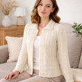 Woman wearing a cream cable knit cardigan sitting on a couch in a cozy living room.